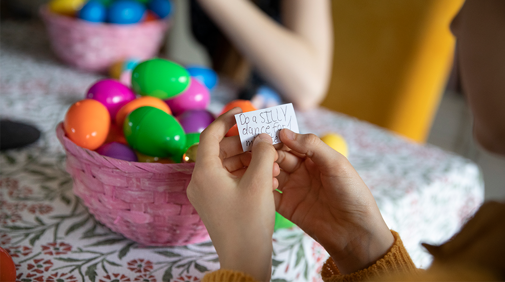 Child holding a piece of paper with written instructions for an activity, found inside one of the multi coloured plastic Easter eggs
